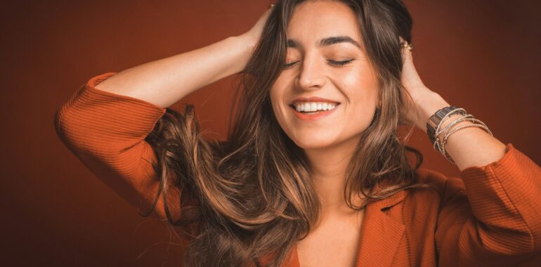 smiling woman in brown top holding hairs