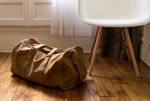 brown duffel bag beside white and brown wooden chair