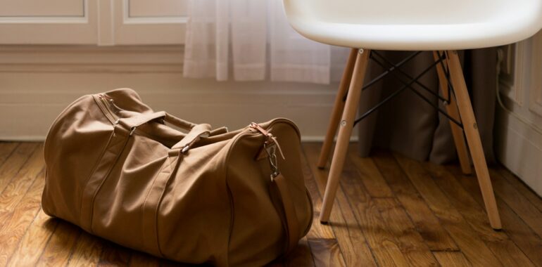 brown duffel bag beside white and brown wooden chair